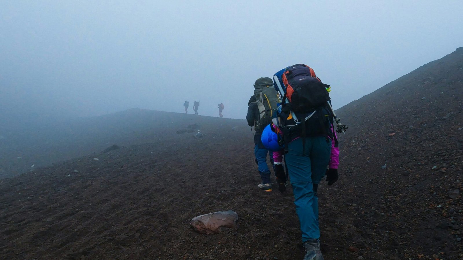 a group of people hiking up a hill on a foggy day